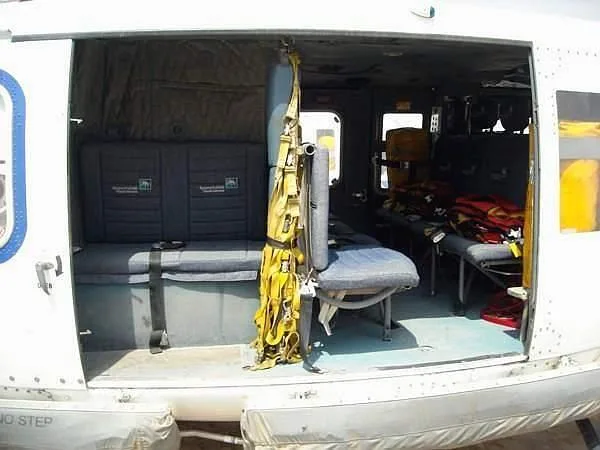The interior of a helicopter cabin showing grey bench seats, a yellow harness, and red life vests.