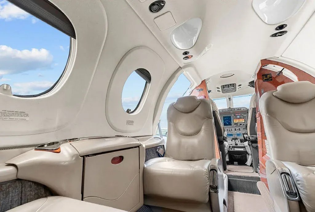 A view from the private jet cabin looking forward into the cockpit, showing beige seats and large windows.