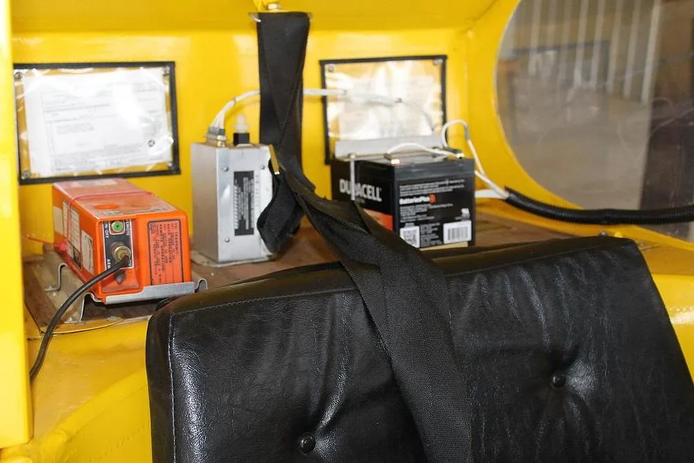 The interior of the yellow aircraft showing a black seat, a Duracell battery, and other equipment in the rear cabin.