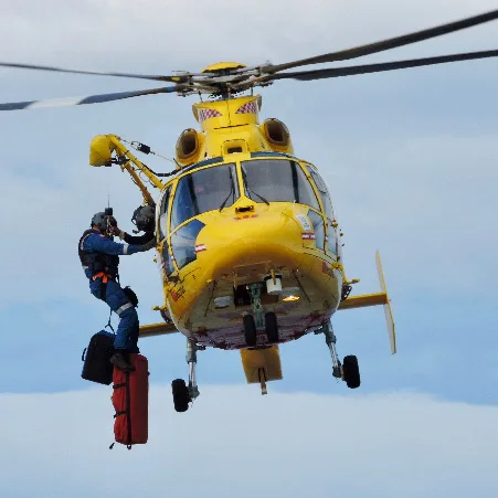 A yellow helicopter with a rescue worker hanging from it.