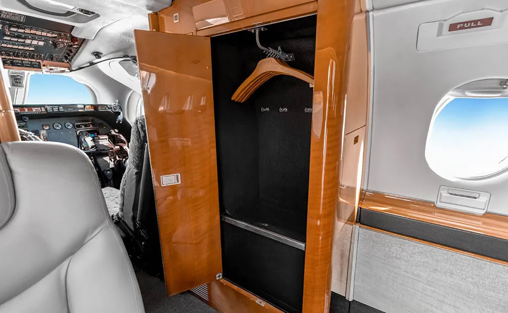 An open wood-paneled closet with a hanger is visible in the aircraft cabin, with the cockpit in the background.