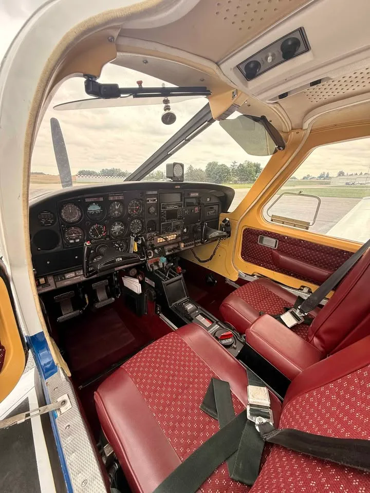 A view into the cockpit of the N4921W aircraft, showing the instrument panel, controls, and red seats.