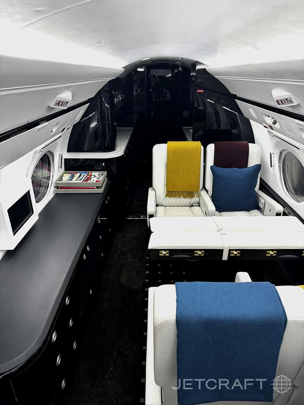 A view of the private jet's cabin interior, showing white seats with colorful throws and pillows, and a dark console table.