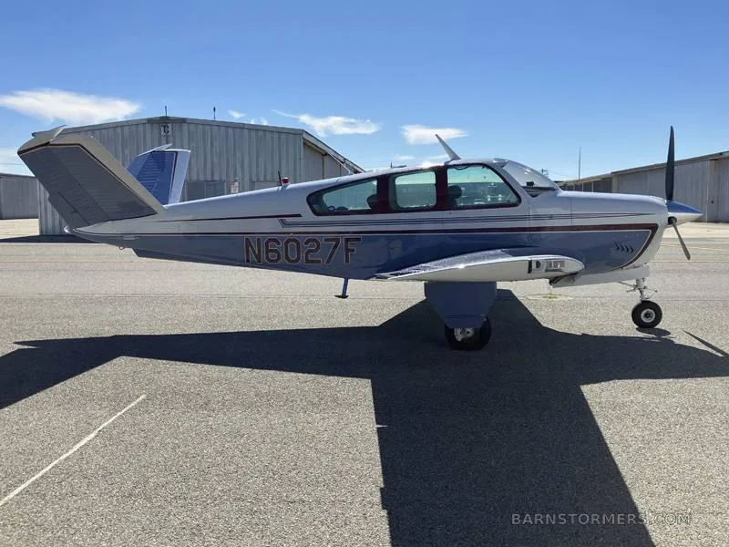 A light blue and white single-engine aircraft with registration N6027F is parked on an asphalt tarmac, viewed from the right side.