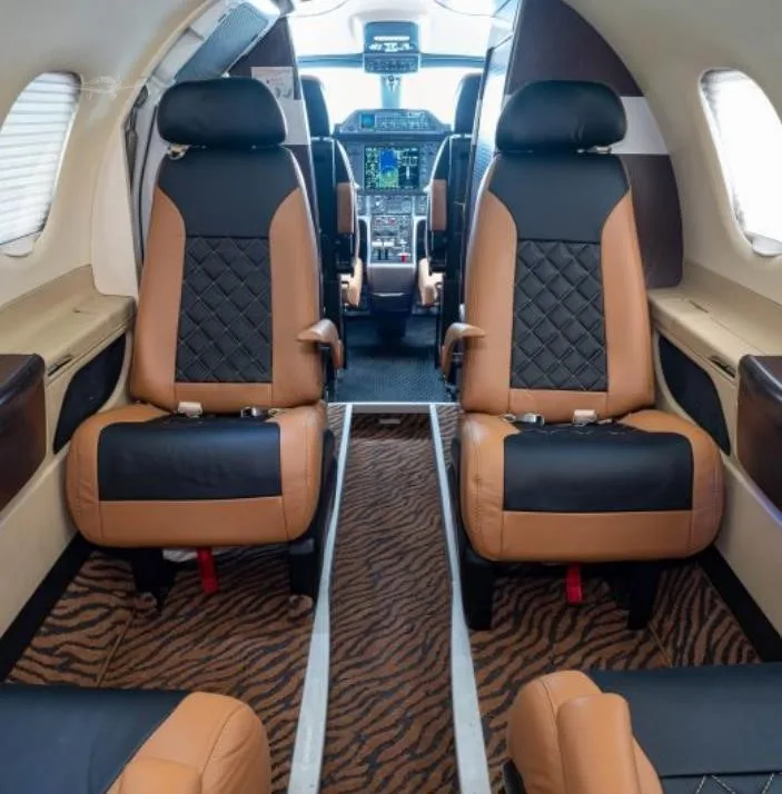 The interior cabin of an Embraer Phenom 100, featuring two-tone tan and black quilted leather seats and a tiger-stripe patterned aisle carpet.