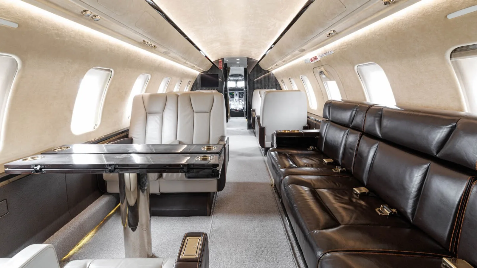 A view down the aircraft cabin aisle, showing a cream leather club seating arrangement with a table and a dark brown leather divan.