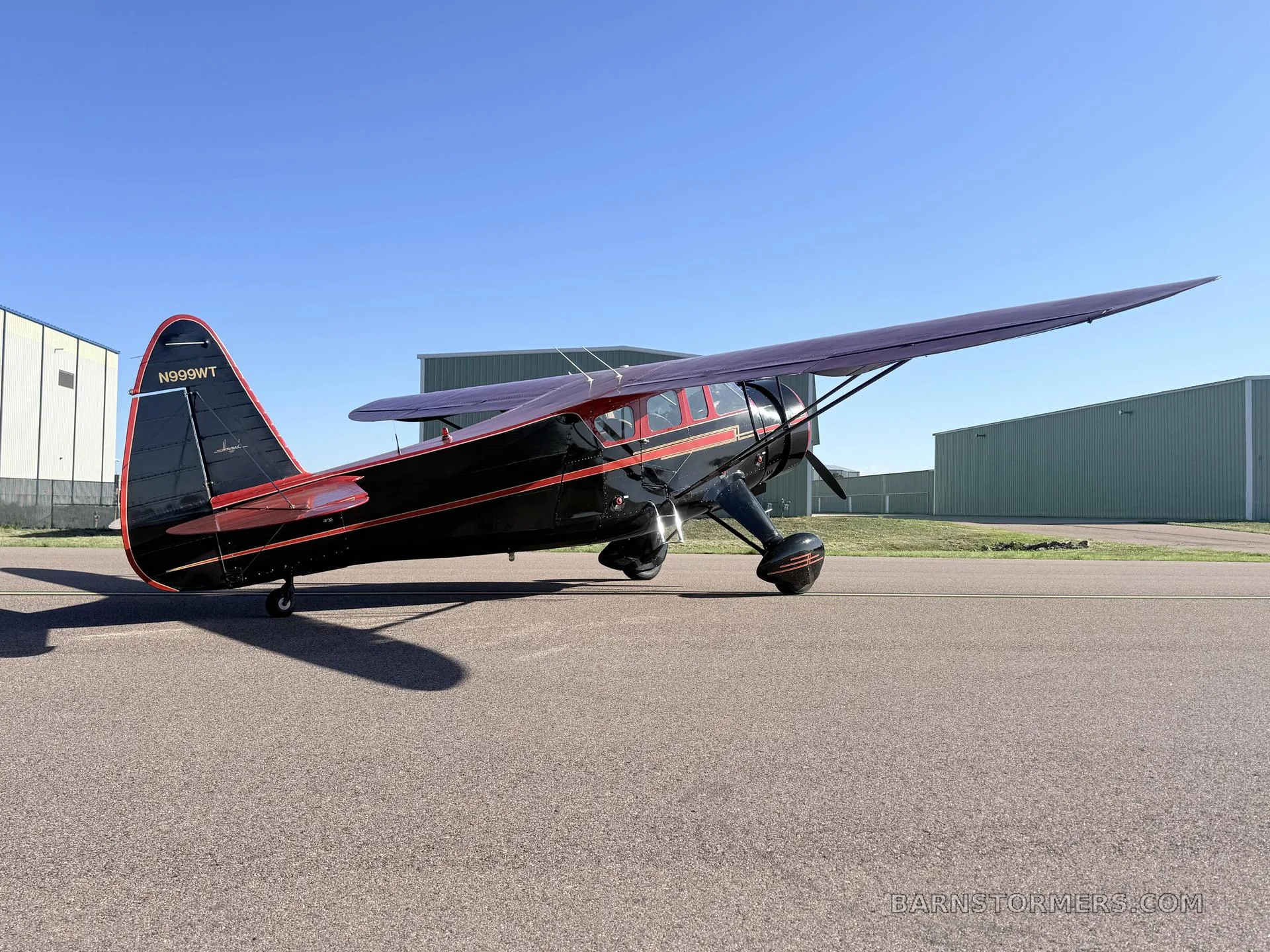 A three-quarter rear view of a black and red vintage high-wing monoplane with tail number N999WT, parked on an asphalt runway.