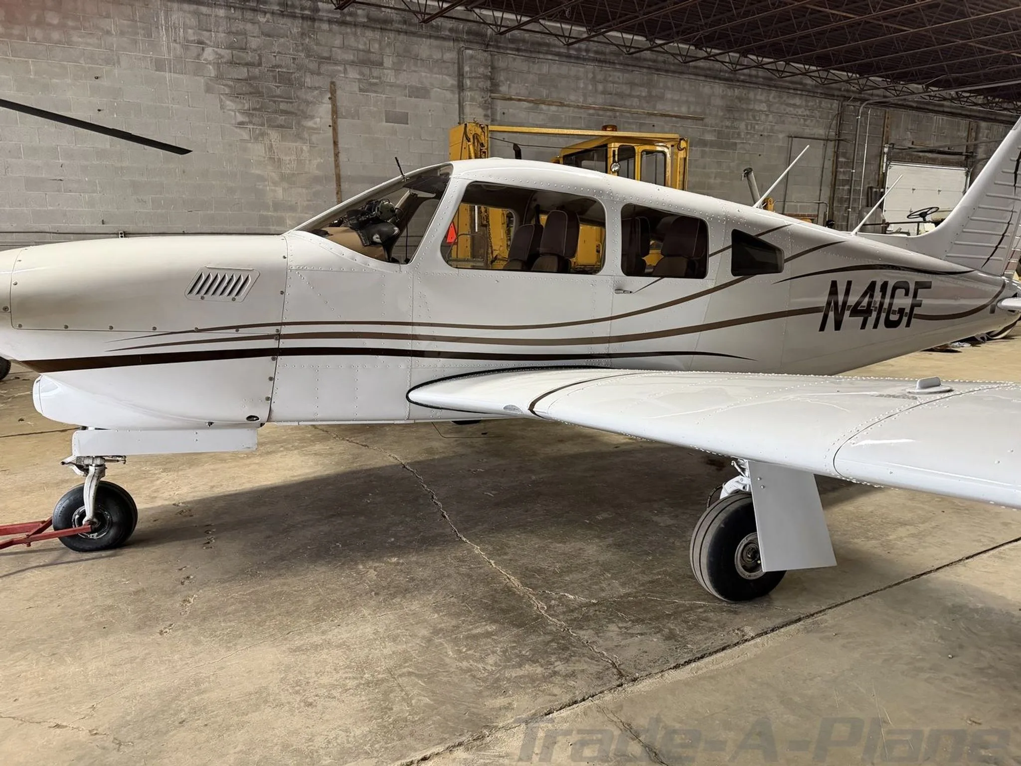 A side view of the white Piper aircraft N41GF with brown stripes, parked in a hangar.