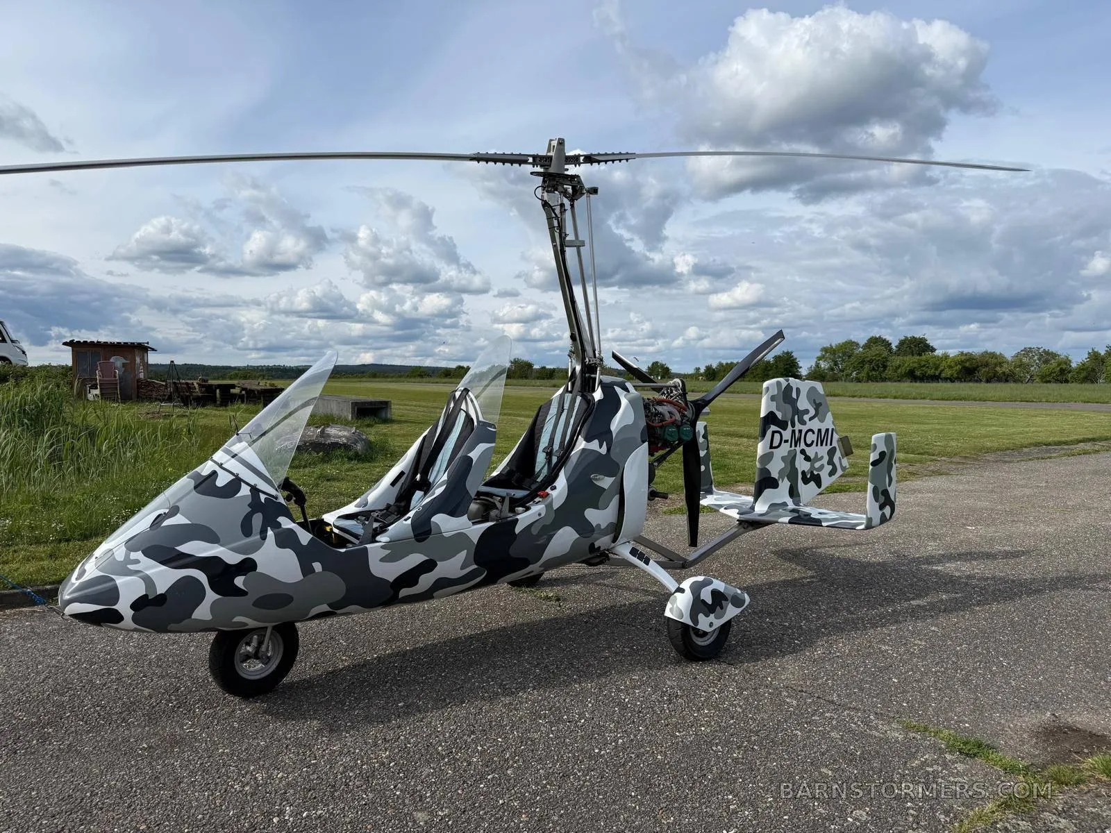 A white and camouflage-wrapped 2011 MTO Sport gyrocopter with registration D-MCMI parked on an airfield under a cloudy sky.