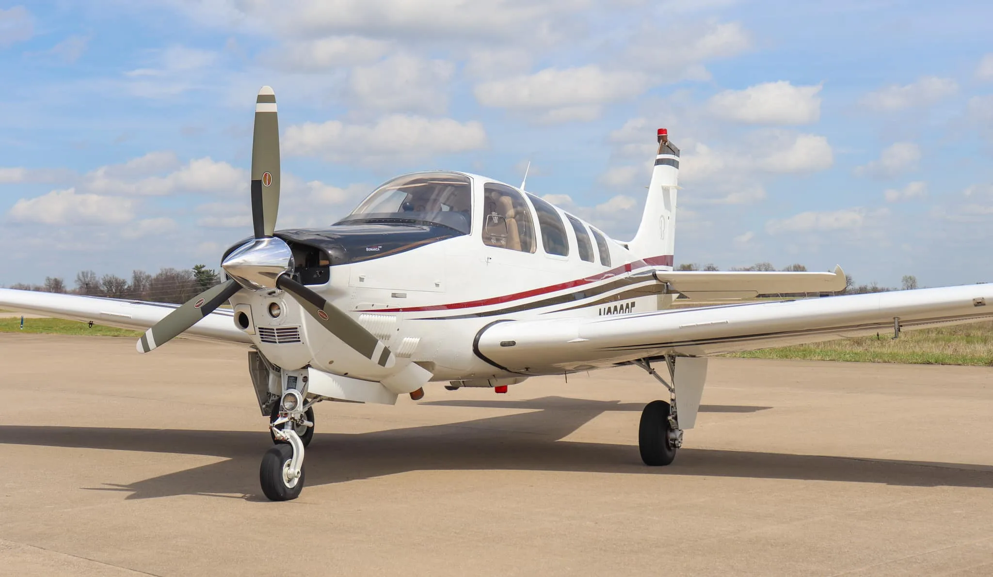 A front-quarter view of a white Beechcraft Bonanza G36 aircraft with a black nose and propeller, parked on an airfield.
