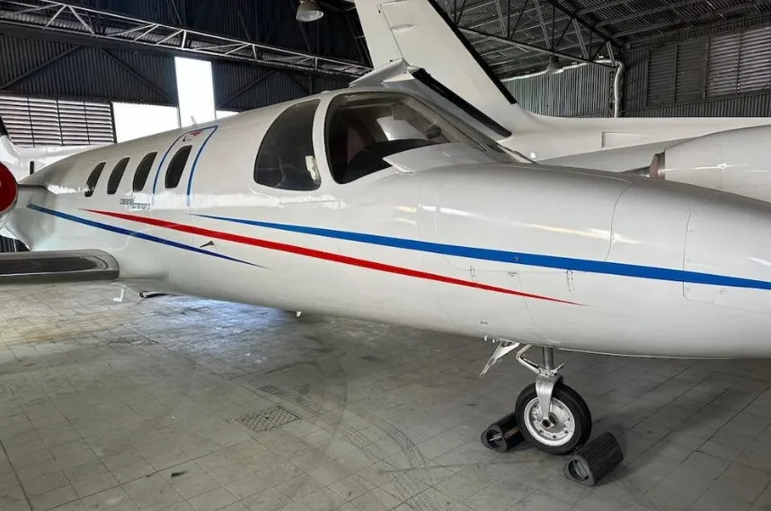A white Cessna Citation jet with red and blue stripes on its fuselage, parked inside a hangar.