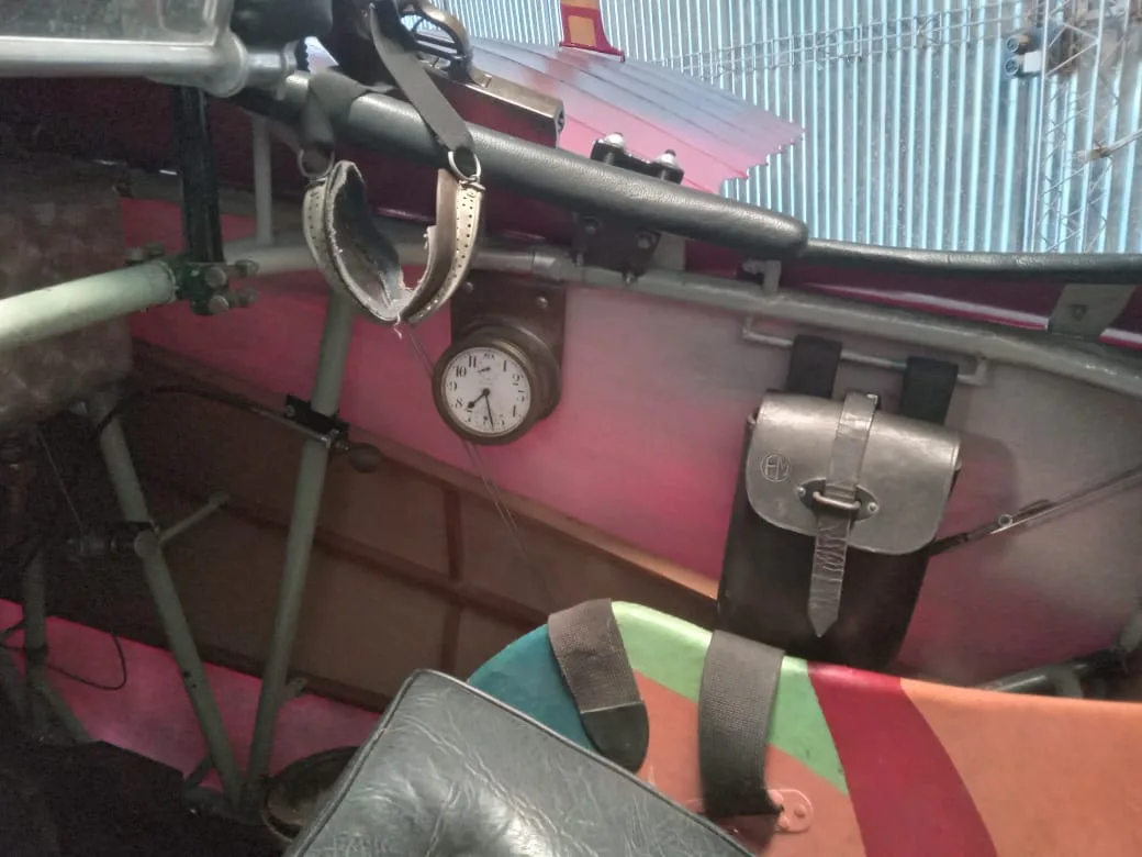 A close-up of the vintage cockpit interior of a triplane, showing a clock and a leather pouch on the side panel.