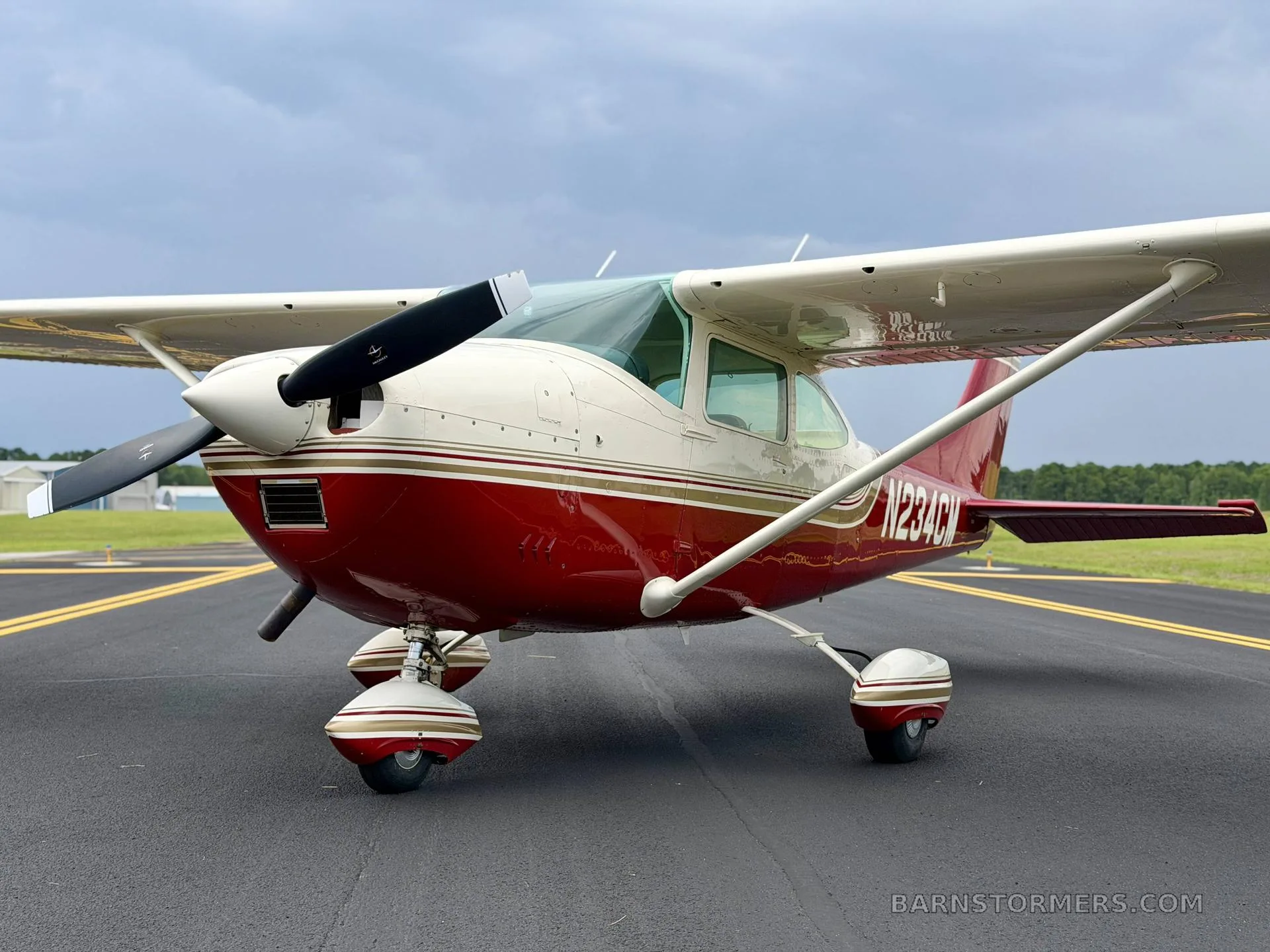 A front-quarter view of a red and white single-engine high-wing aircraft with registration N234CM parked on an airfield.
