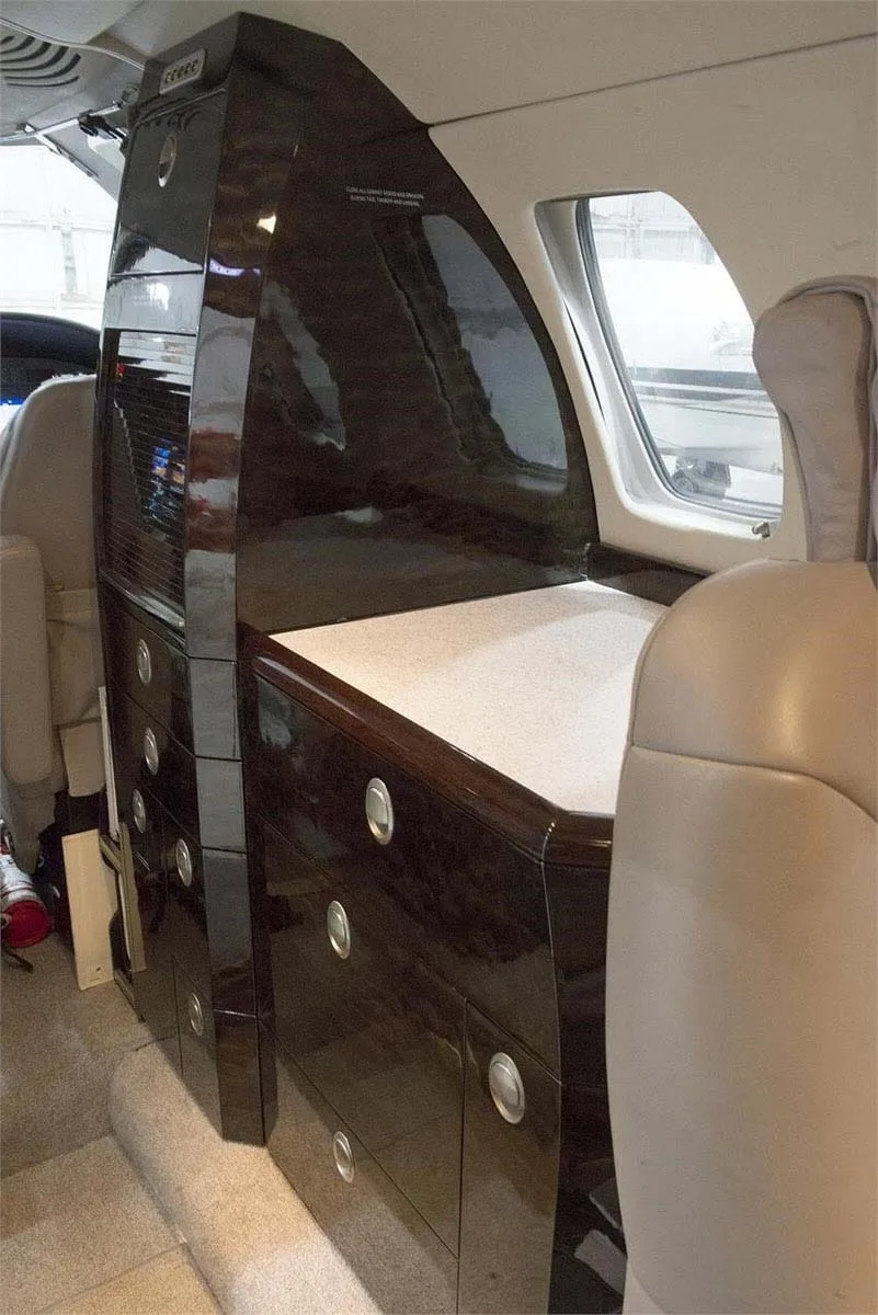 A dark wood-paneled galley or storage cabinet area inside a private jet cabin.