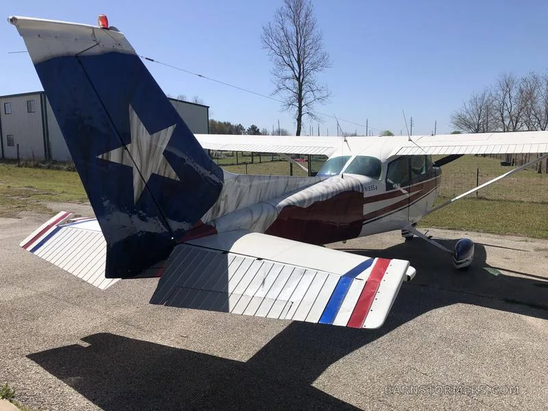 A rear view of a Cessna 172 showing its tail painted with a large white star on a blue background, parked on asphalt.