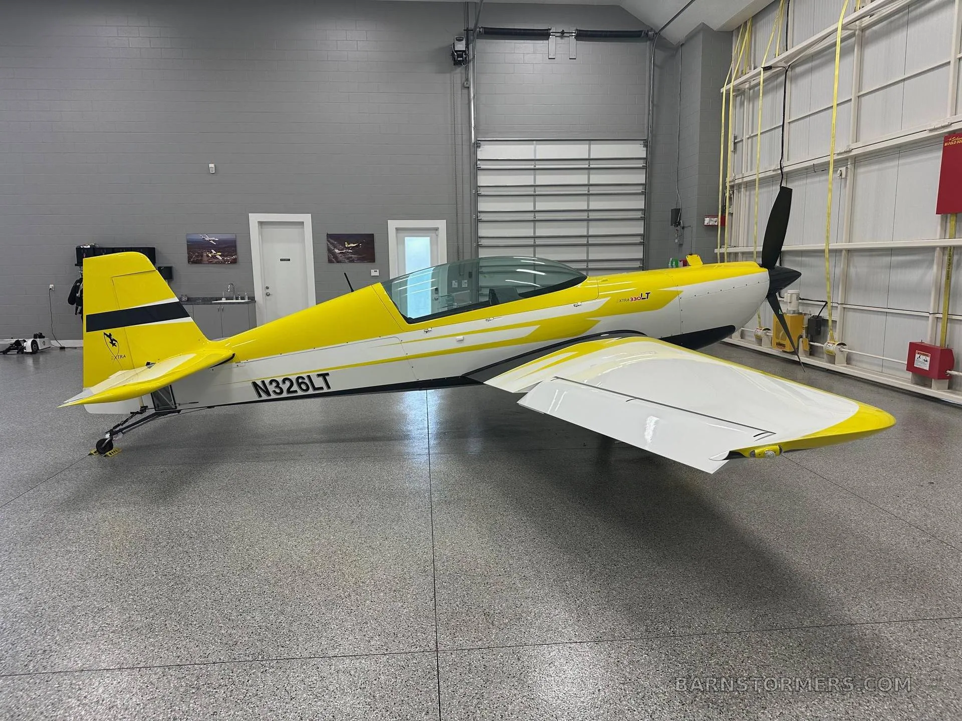 A yellow and white Extra 330LT aerobatic aircraft with registration N326LT, viewed from the left side in a hangar.
