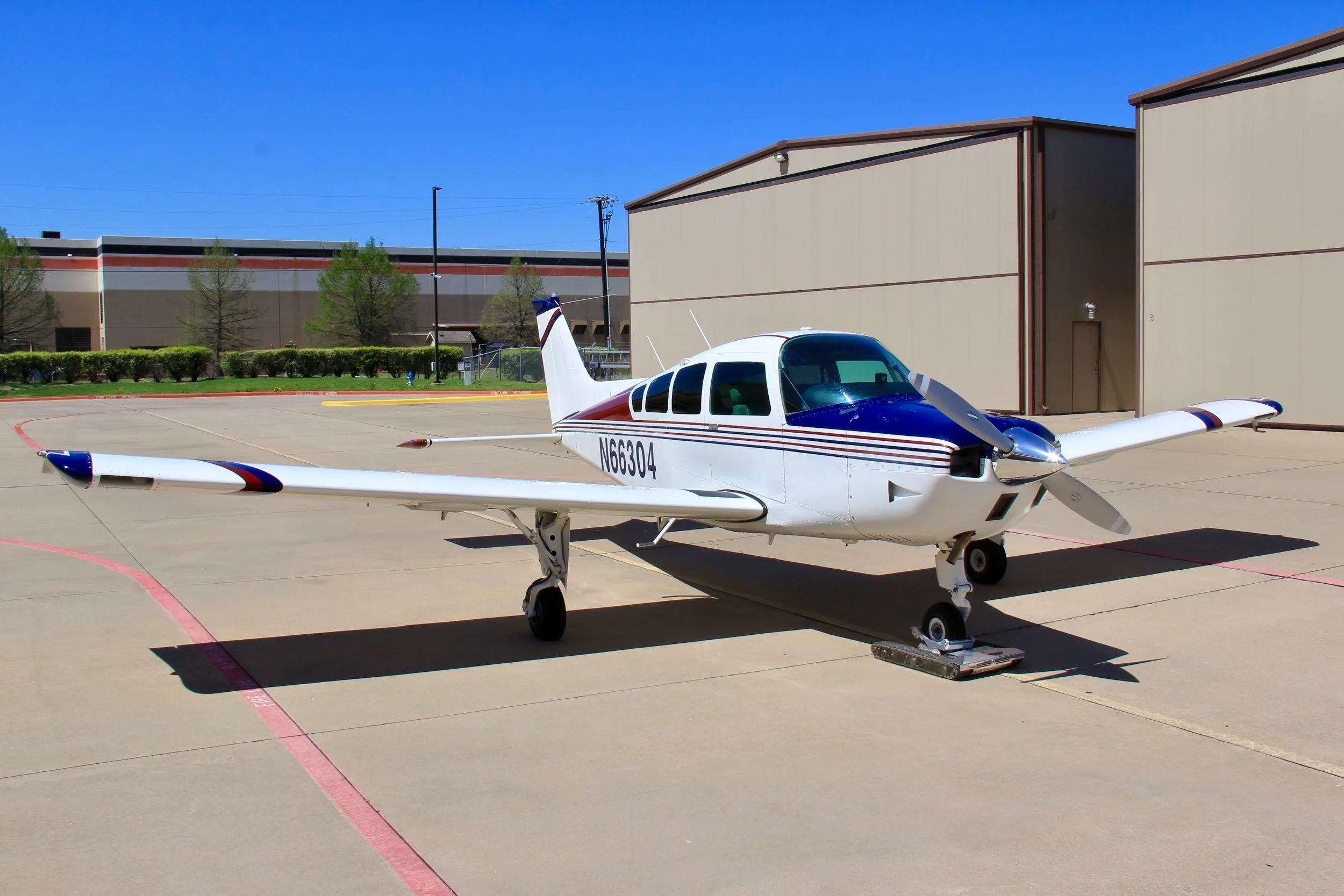 A three-quarter front view of the white, blue, and red single-engine aircraft (N66304) on an airport tarmac.