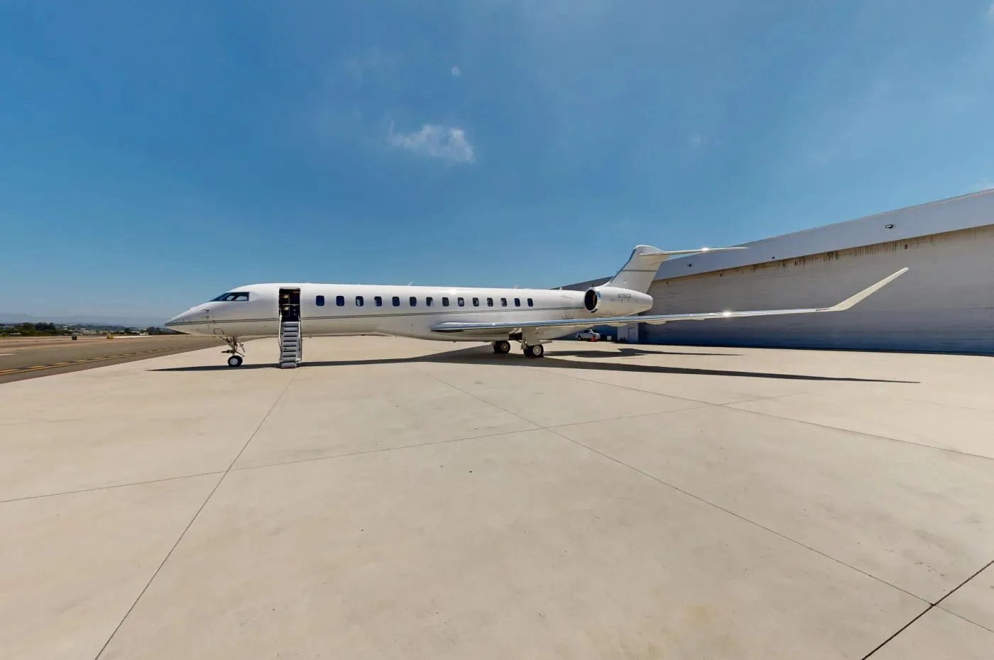 A white business jet with its door open and stairs extended, parked on a tarmac next to a hangar under a clear blue sky.