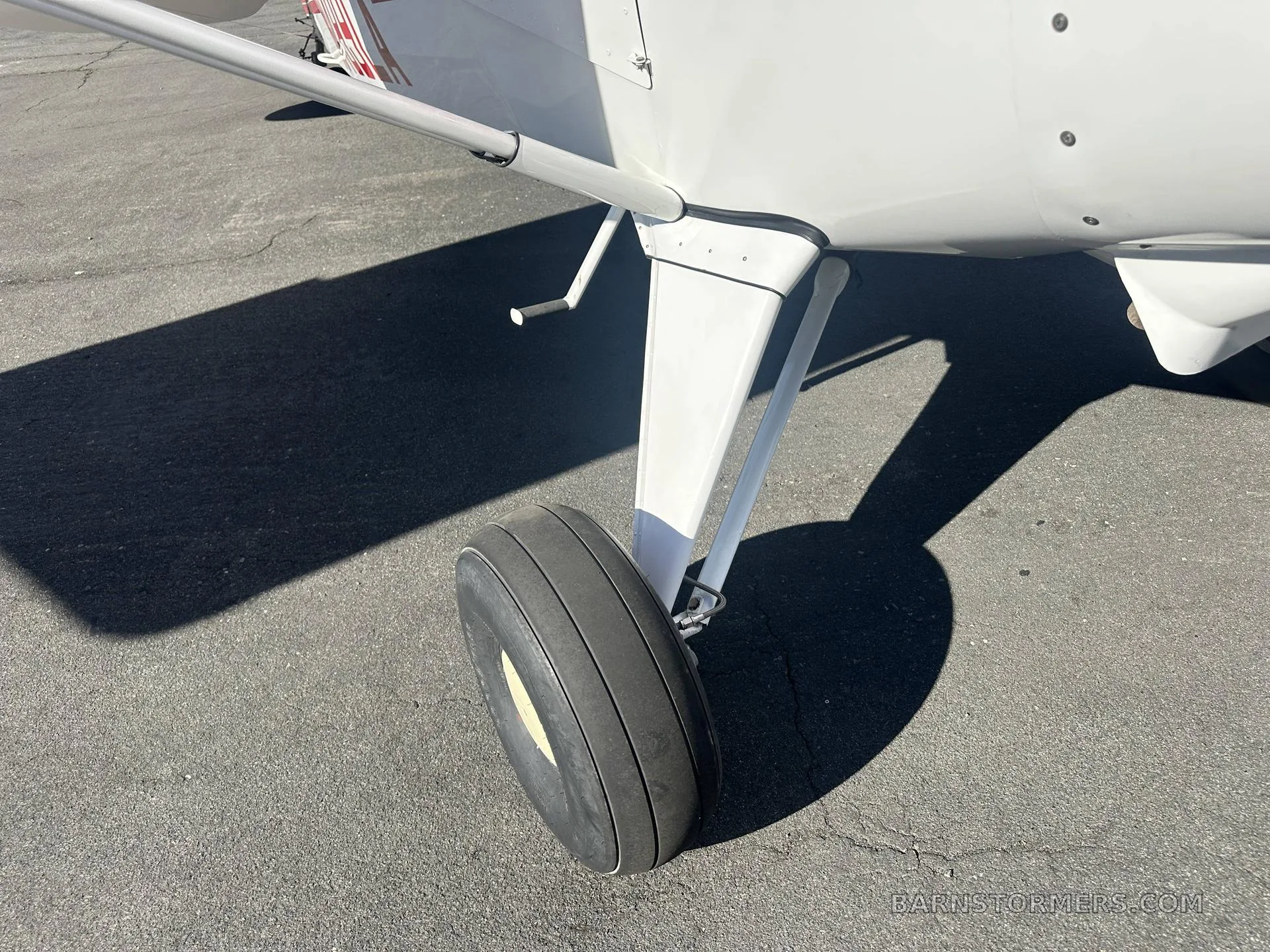 A close-up view of the main landing gear and tire of a white Maule M-7-235 aircraft on an asphalt surface.