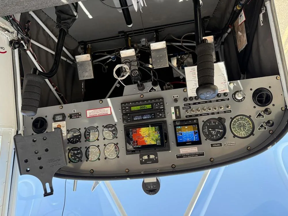 The aircraft cockpit features a grey instrument panel with analog gauges, digital displays, and flight controls.