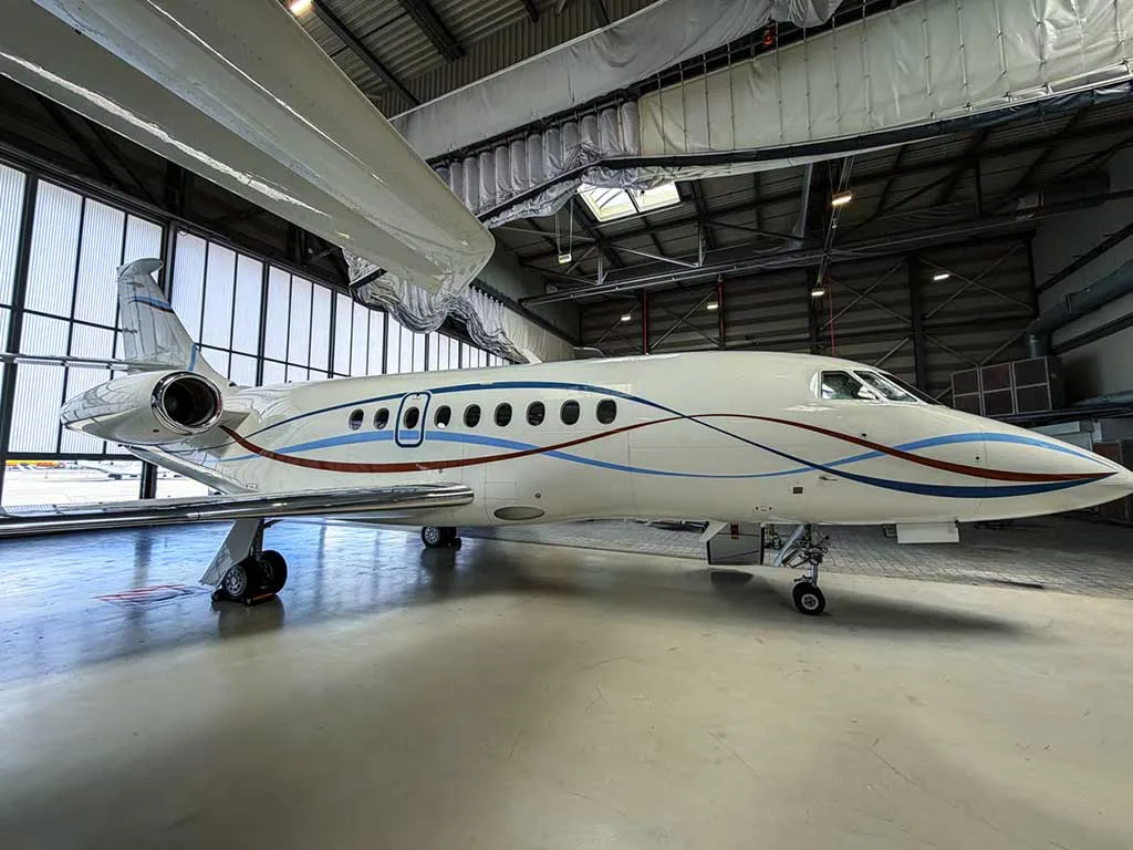 A white business jet with blue and red wavy stripes on its fuselage, parked inside a hangar.