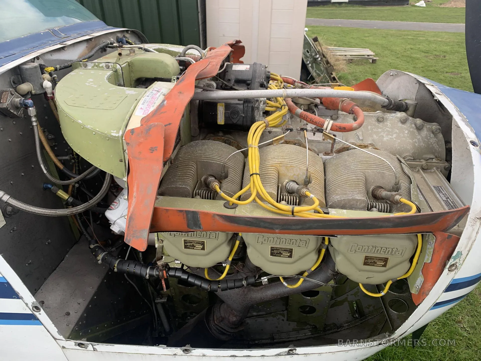 An overhead view of an aircraft's exposed Continental engine with yellow ignition wires and cylinders, parked on grass.