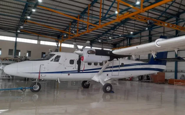 A white twin-engine turboprop aircraft with blue stripes is parked inside a hangar.
