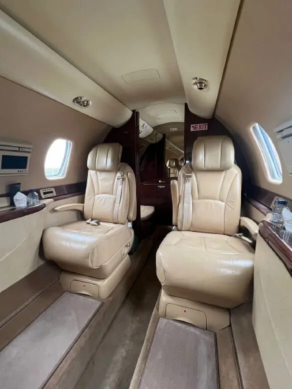 A view down the aircraft cabin aisle shows two pairs of tan leather seats and a dark wood partition at the rear.