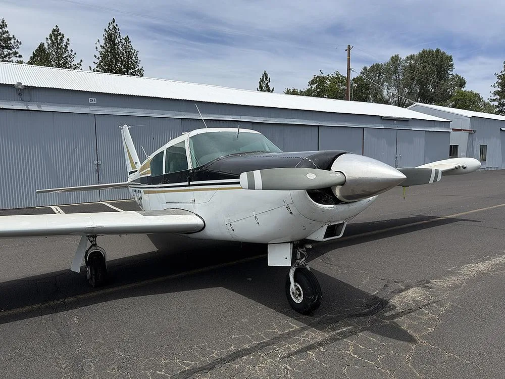 A Piper Comanche 250, registration N5365P, in white and black with gold stripes, parked on an airfield.