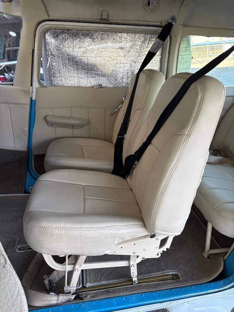The cream-colored front passenger seats with black shoulder harnesses in the aircraft cabin.