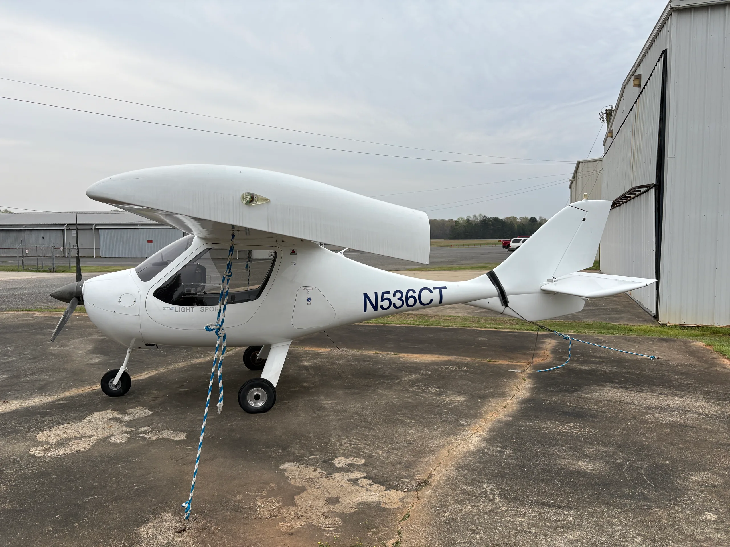 A white light sport aircraft, N536CT, is seen from the right side, parked on a tarmac next to a hangar.