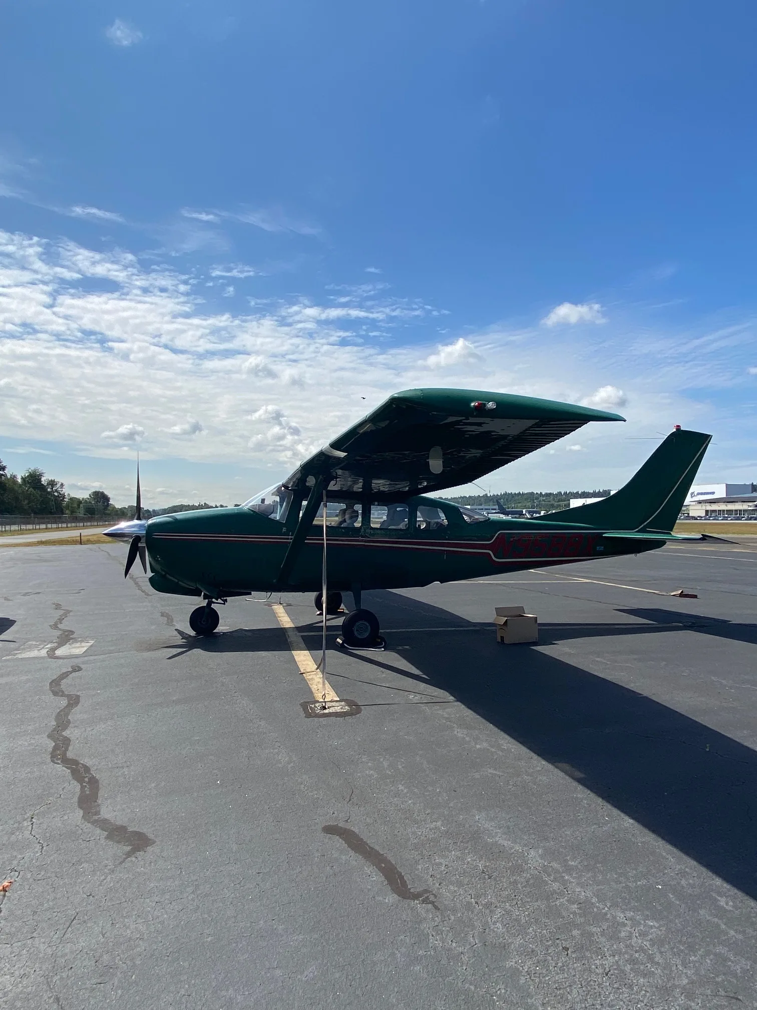 A green Cessna 210 aircraft with red and white stripes parked on an airfield under a blue sky.