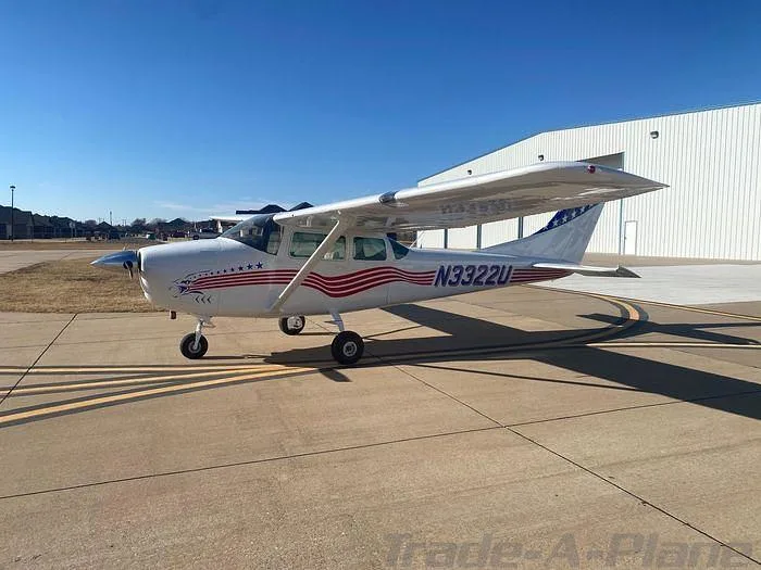 A white Cessna 172 with patriotic red and blue stripes is parked on an airport tarmac.