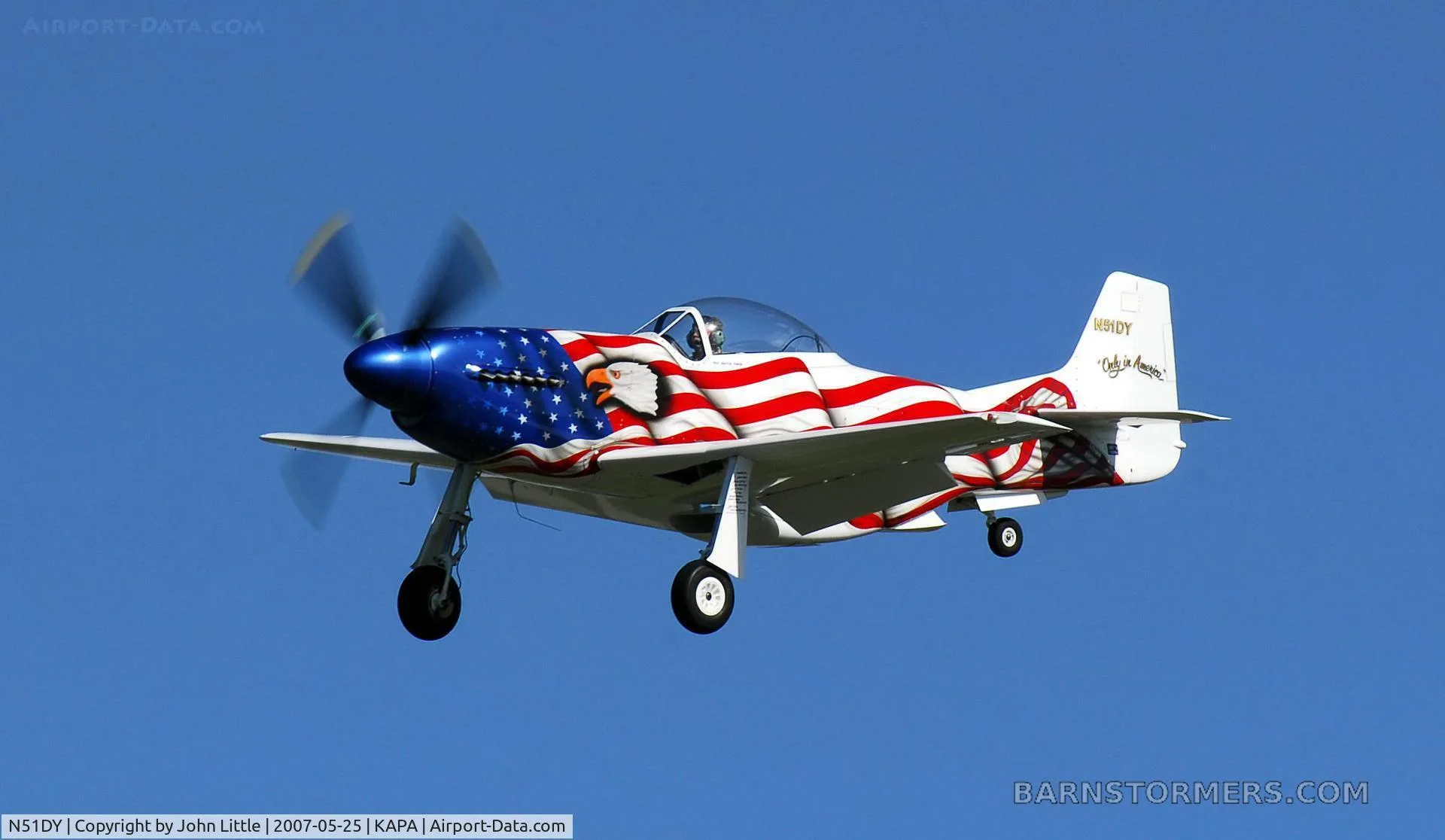 A P-51 Mustang replica, painted with an American flag and eagle, flying against a clear blue sky.