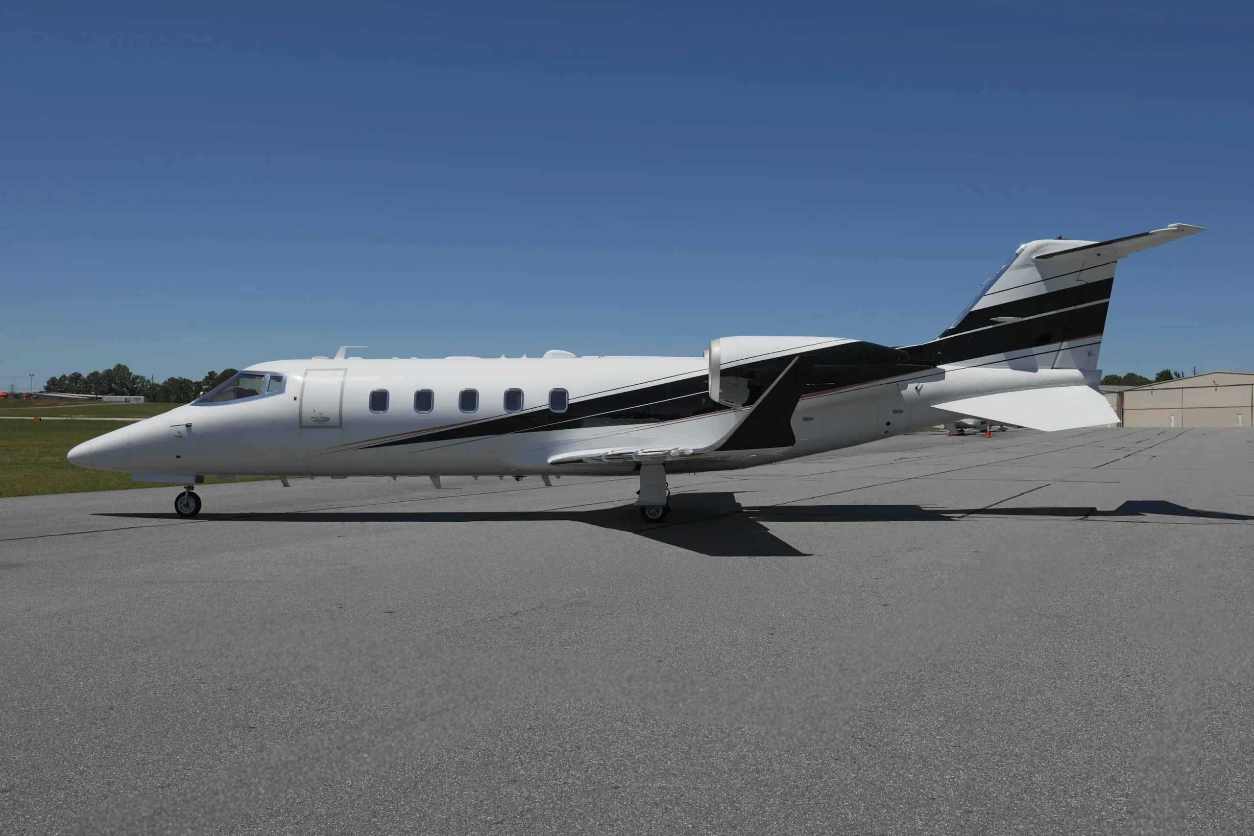 A white business jet with black and gold stripes, parked on an airport tarmac under a clear blue sky.