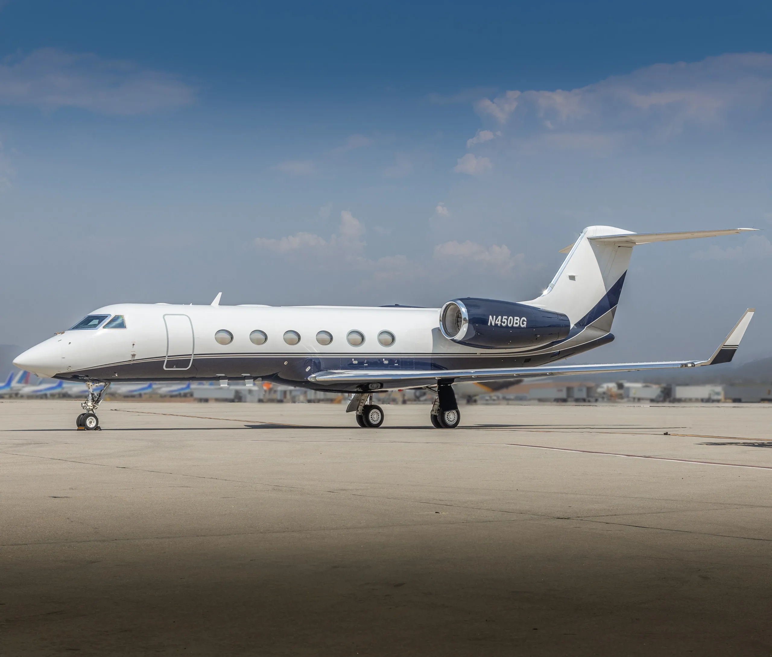 A white and dark blue Gulfstream business jet with tail number N450BG is parked on an airport tarmac under a blue sky.
