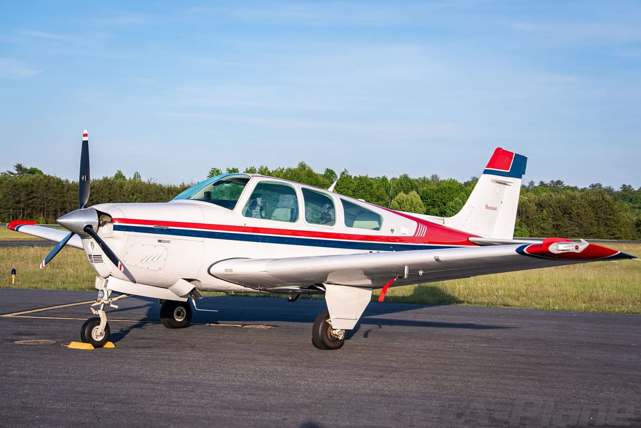 A side view of the white, red, and blue Beechcraft Bonanza N3108N parked on an asphalt ramp.