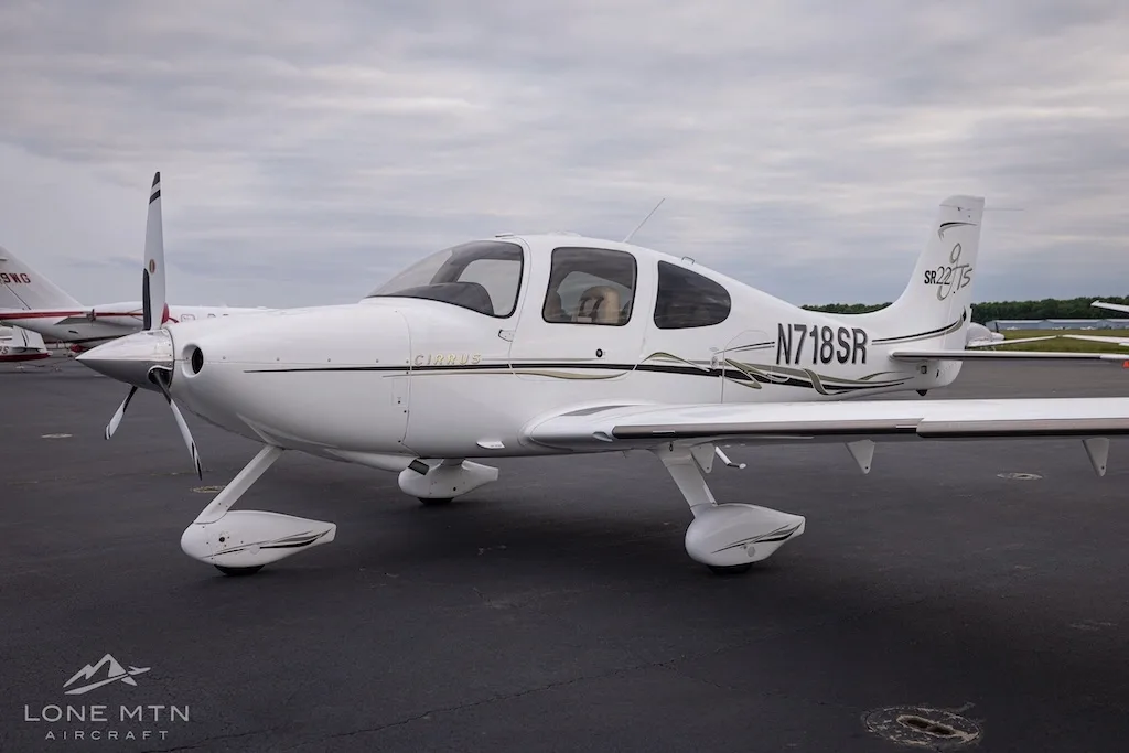 Front-side view of a white Cirrus SR22T aircraft with black and gold accents parked on an asphalt tarmac.