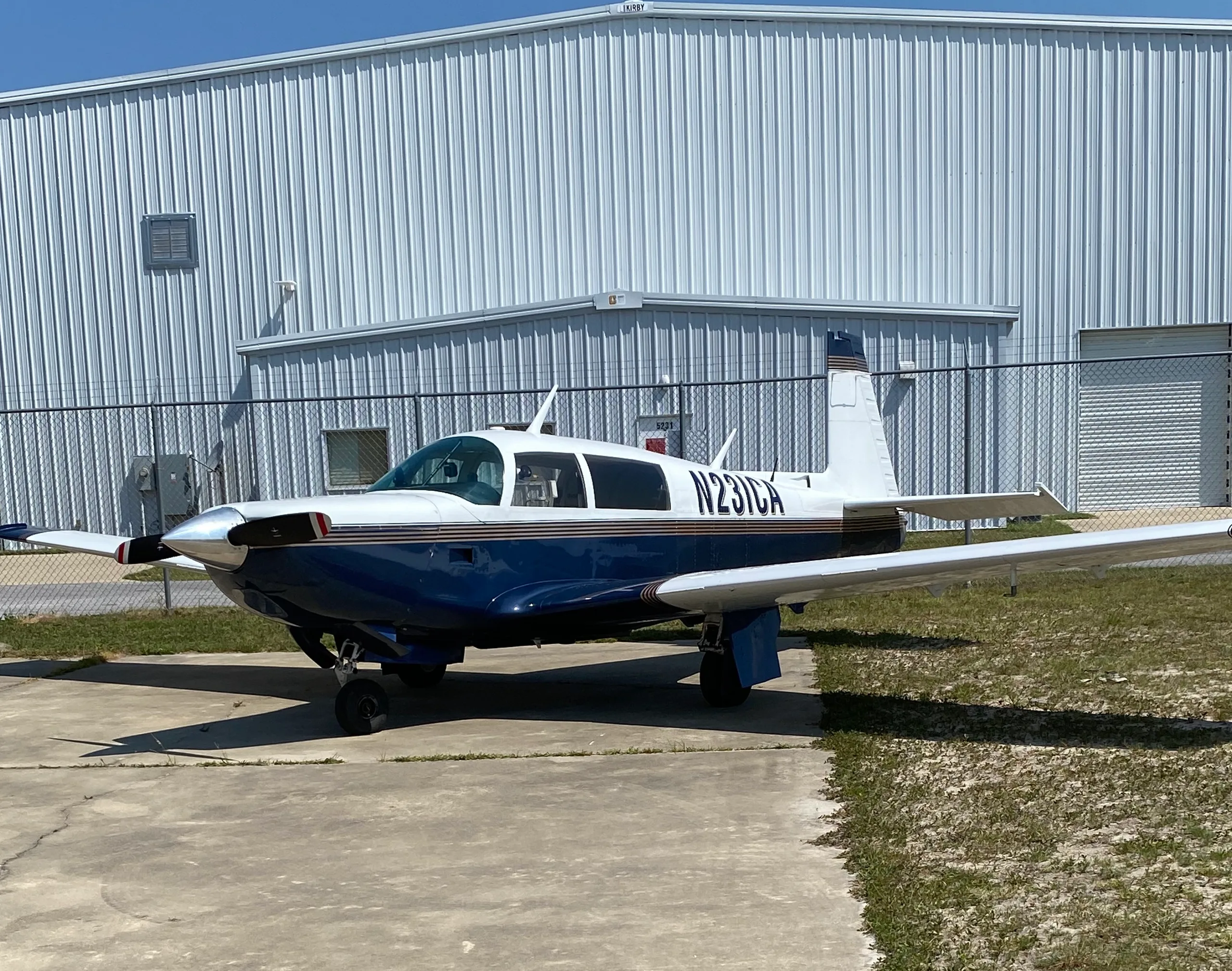 A blue and white single-engine aircraft (N231CA) parked on concrete next to a white hangar.