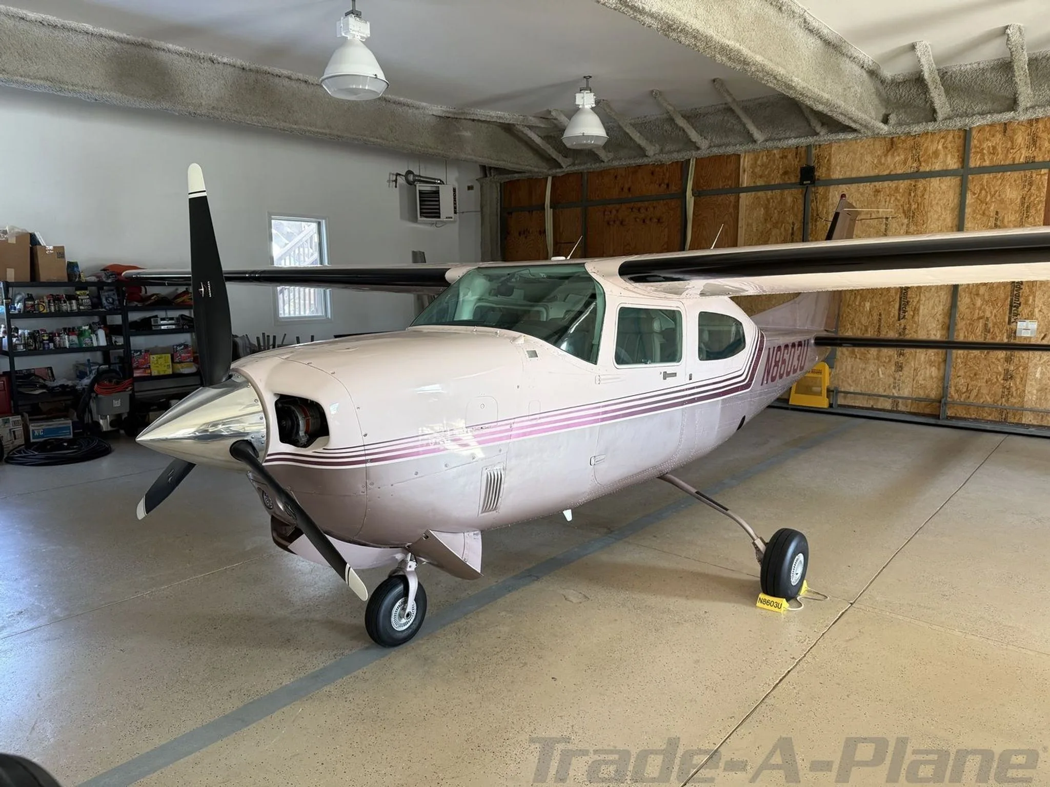 A front view of a light pink and purple Cessna 210 Centurion aircraft, registration N8603U, parked in a hangar.