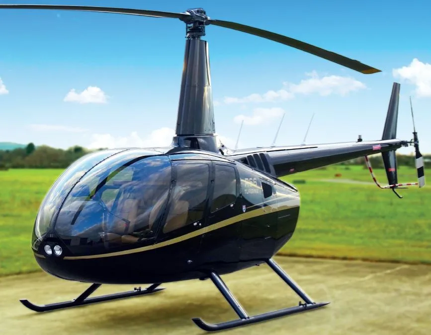 A sleek black Robinson R66 Turbine helicopter with gold stripes, parked on a grassy field under a blue sky.