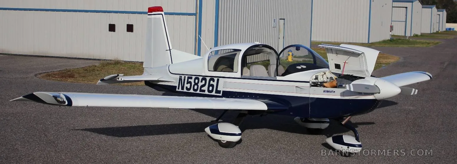 A white and blue Bobcat aircraft (N5826L) parked on an airfield with its canopy and engine cowling open.