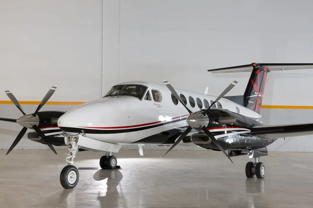 A white and black Beechcraft King Air turboprop aircraft with red accents on the tail and fuselage, parked in a hangar.