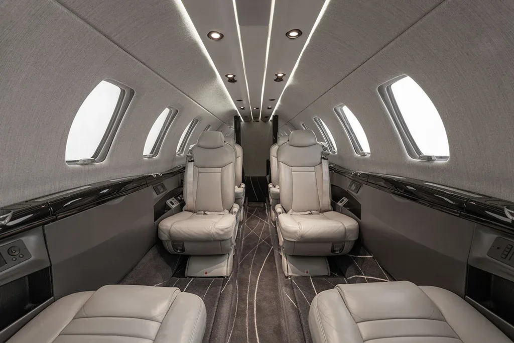 The luxurious interior cabin of a private jet features light gray leather seats and a patterned carpet.