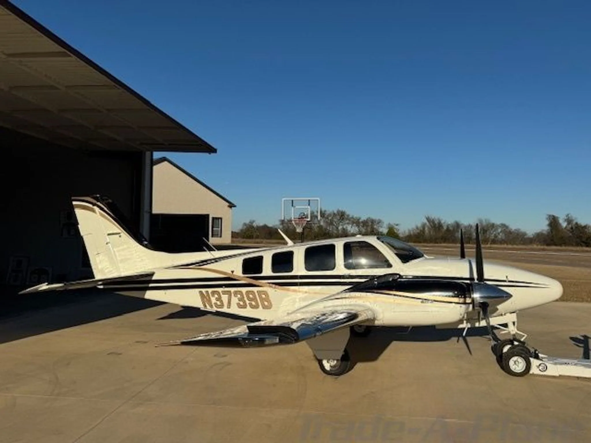 A white and black twin-engine aircraft with gold stripes parked on a tarmac next to a hangar.