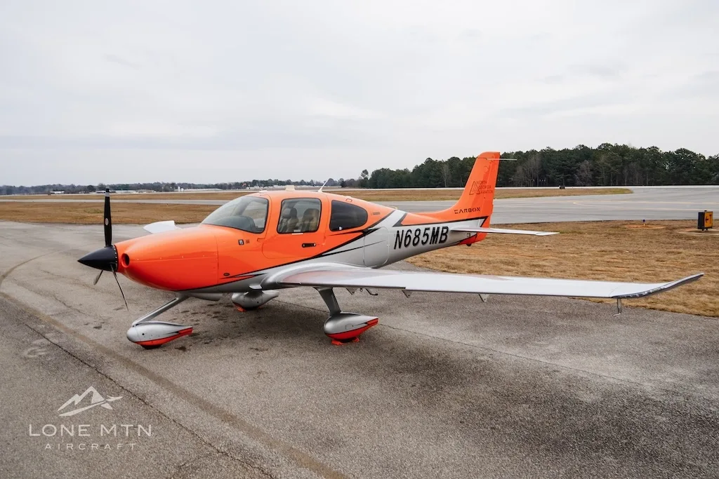 A Cirrus SR20 aircraft with an orange and silver paint scheme parked on an airfield.