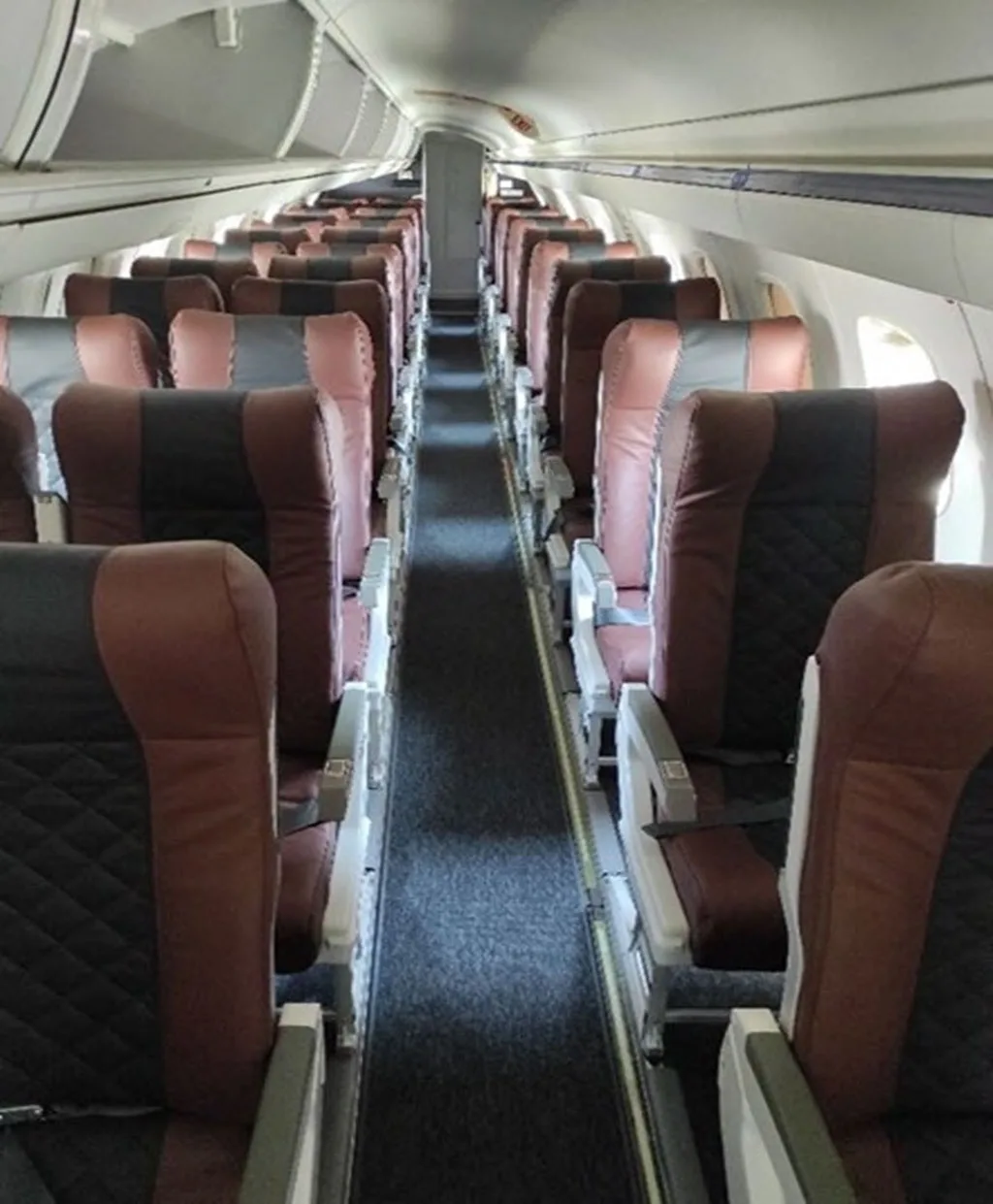 A view down the central aisle of an aircraft cabin, showing rows of brown and black passenger seats.