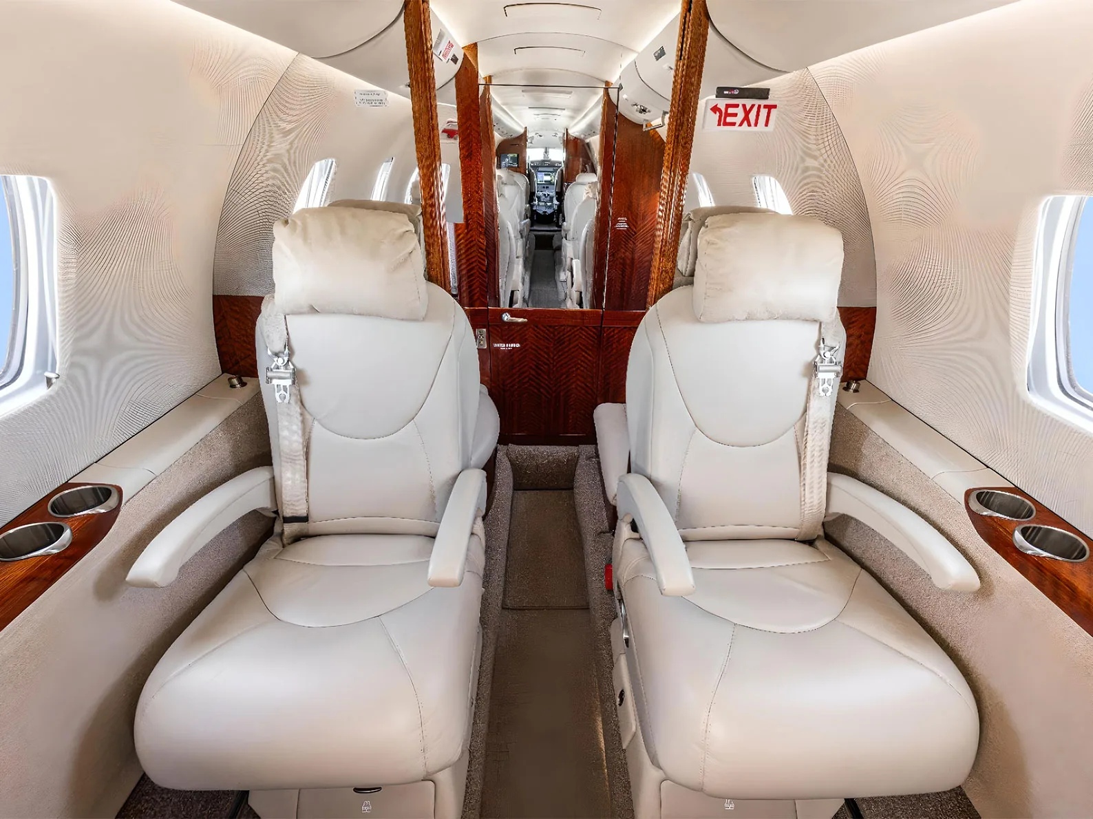 A view down the aisle of a private jet cabin, showing two forward-facing light leather seats and wood paneling.