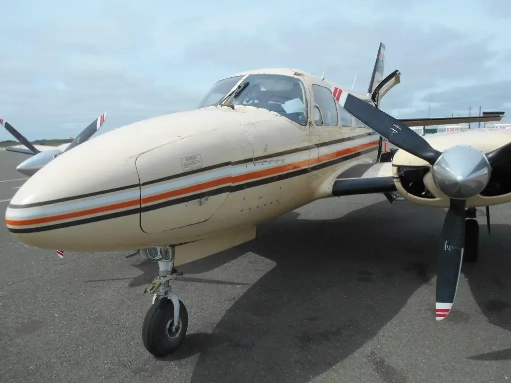 A close-up front-quarter view of the beige twin-engine Piper Navajo aircraft, N4112E, showing the nose and right engine.