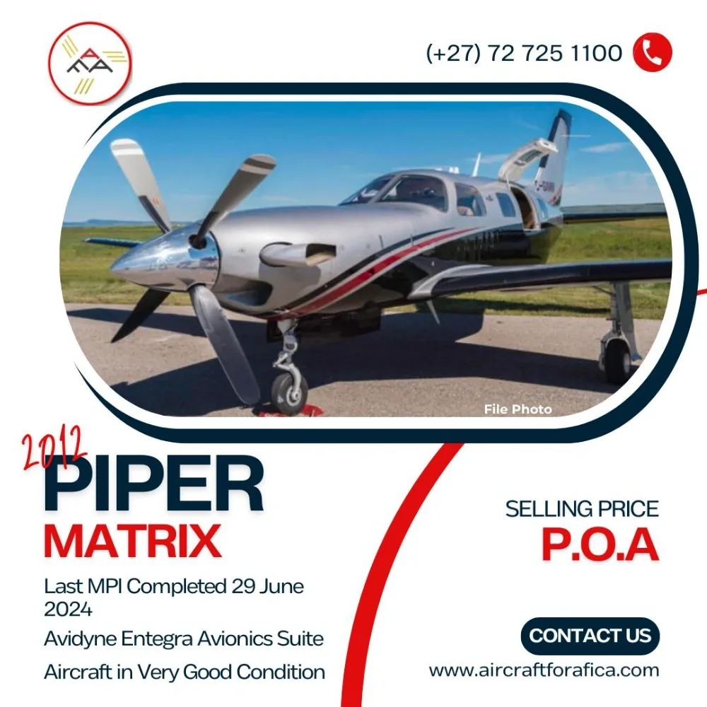 A silver and black Piper Matrix aircraft with an open cabin door is parked on an airfield under a clear blue sky.